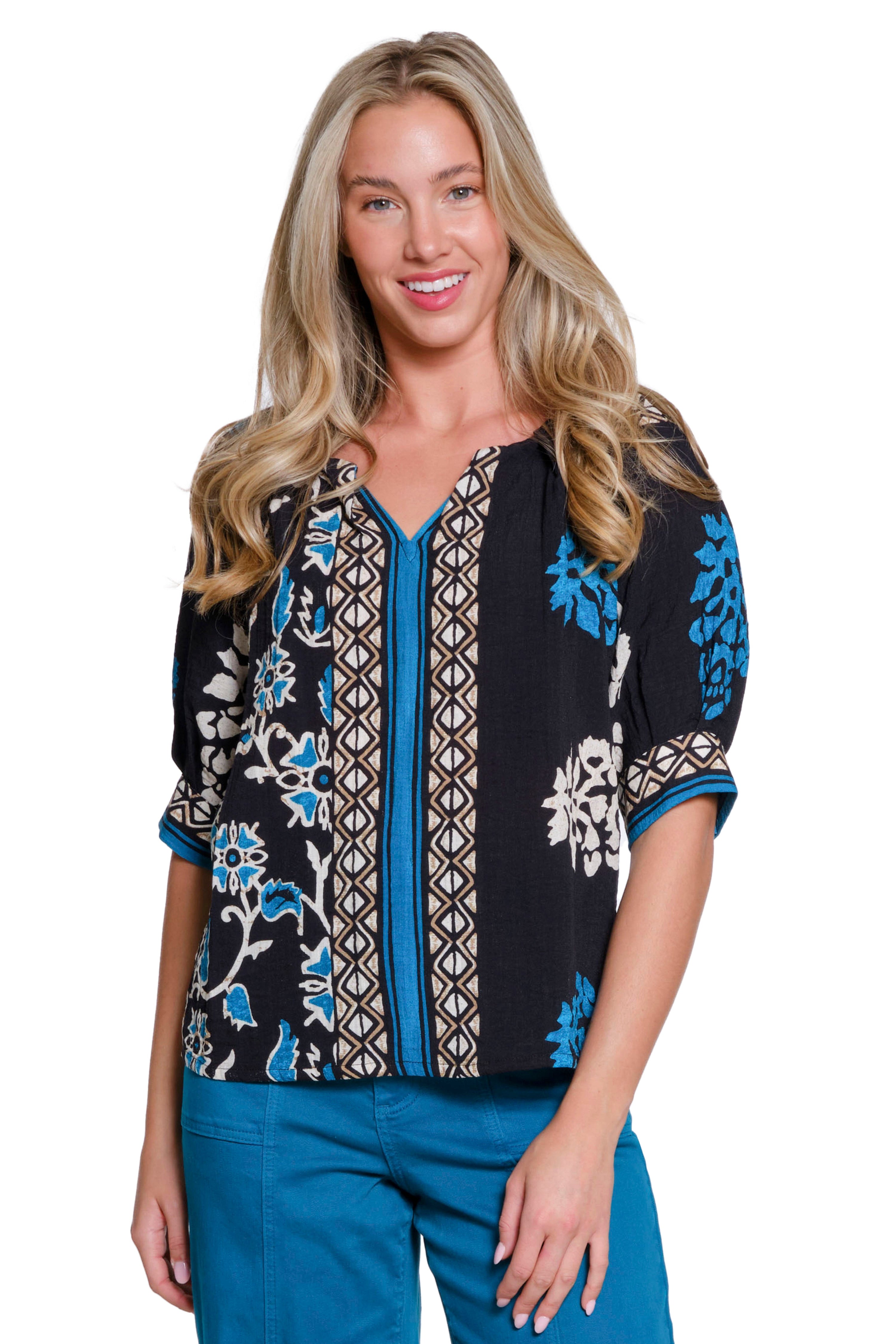 Woman wearing a black floral embroidered top with blue accents on a white background