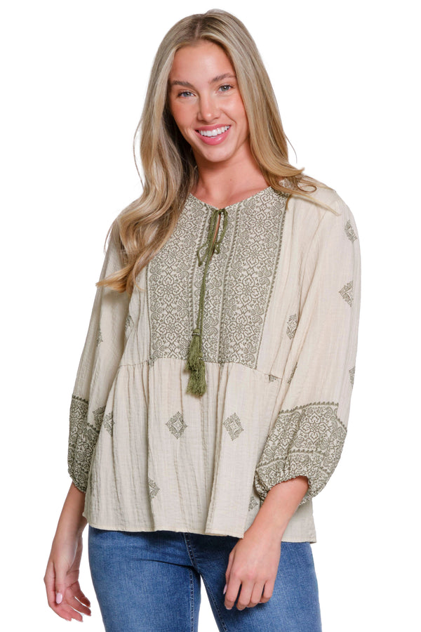 Woman wearing a beige blouse with intricate patterns and blue jeans on a white background