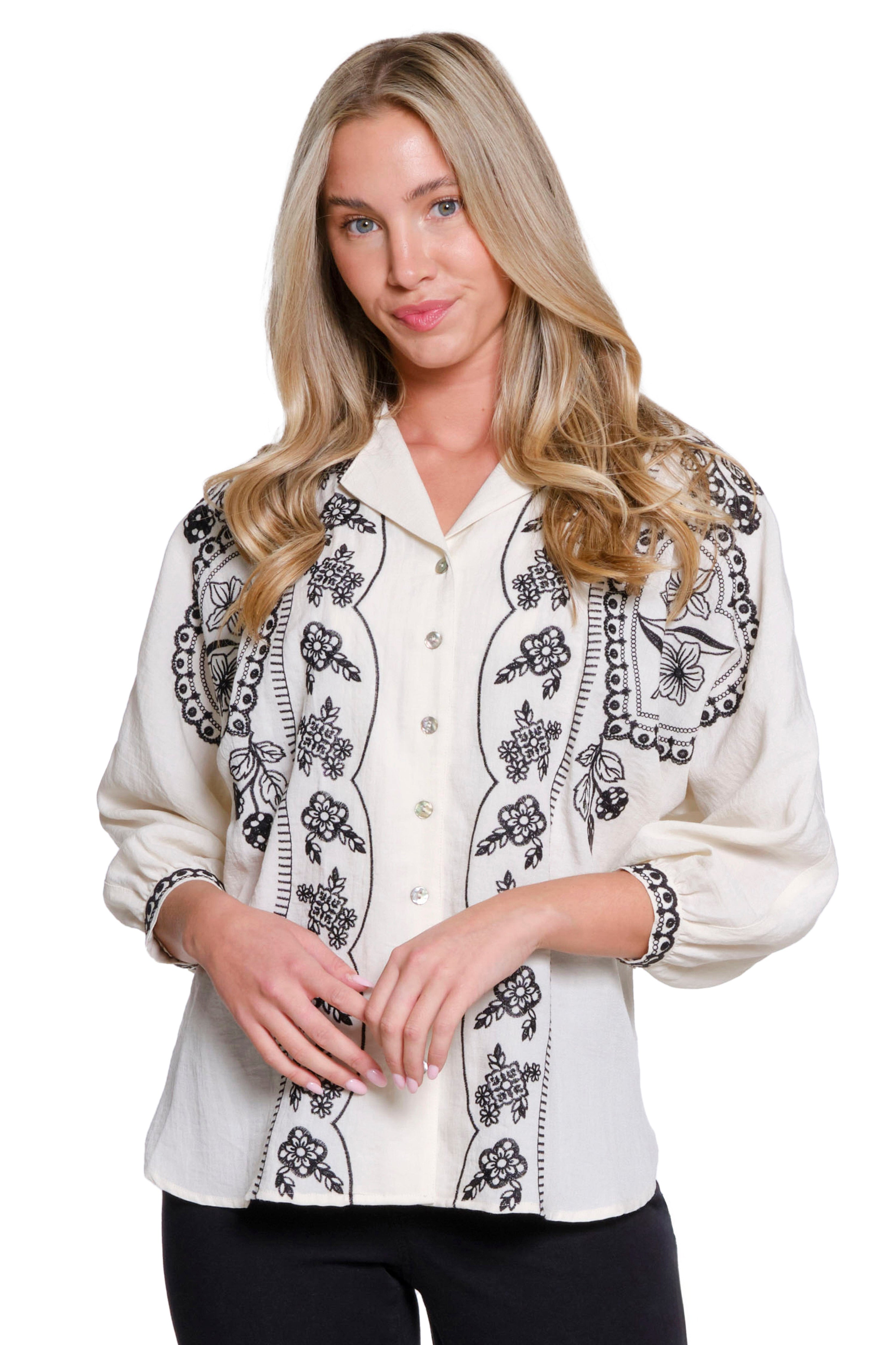 Woman wearing a white blouse with black floral embroidery on a white background