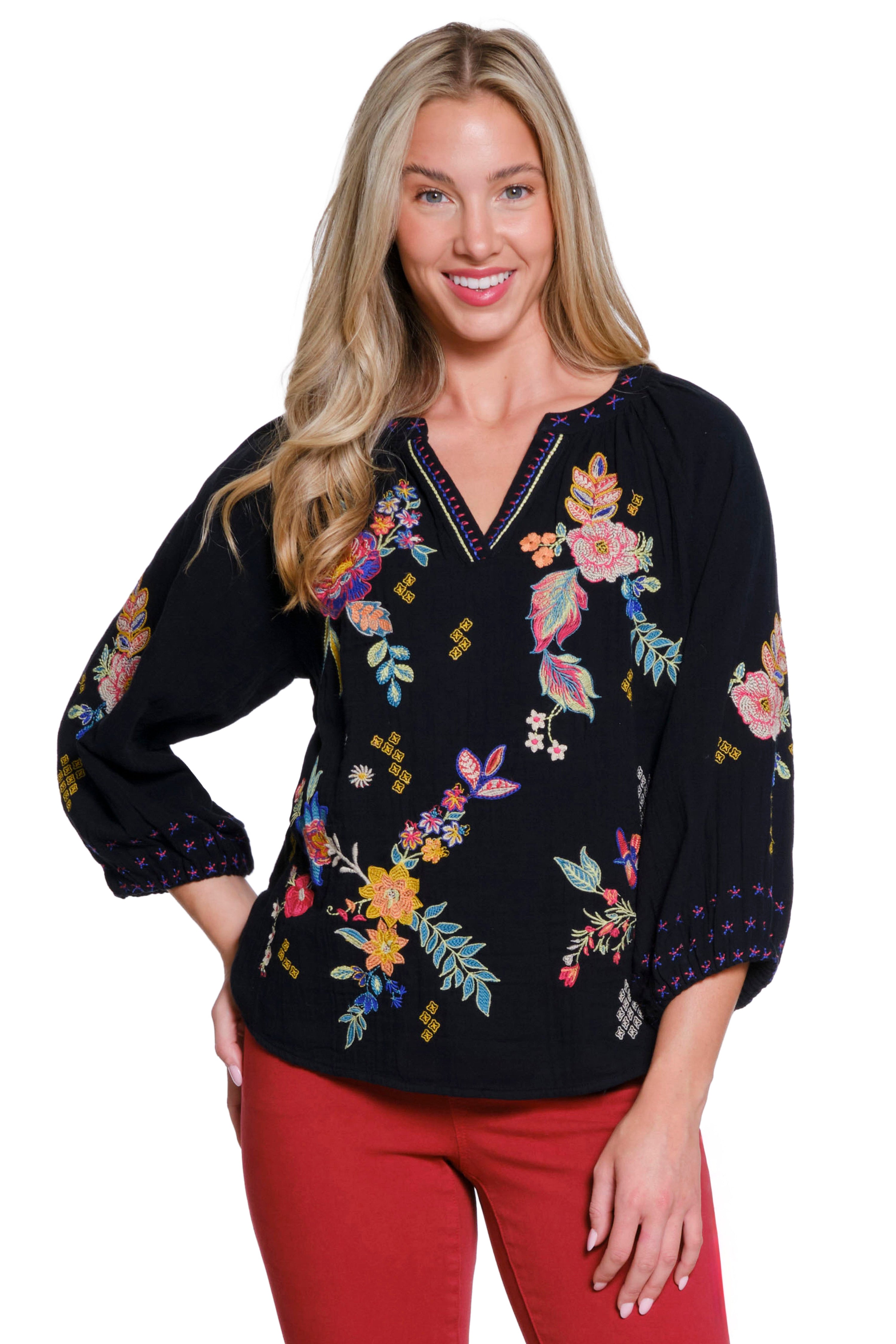 Woman wearing a black floral embroidered blouse with red pants on a white background